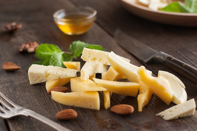 Couper le fromage avec une fourchette et un couteau sur une table en bois sombre