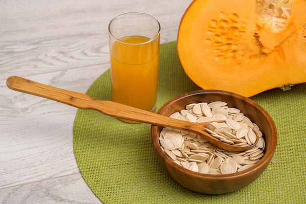 Couper les graines de citrouille dans une tasse en bois avec une cuillère en bois de jus de citrouille dans un verre sur une serviette verte