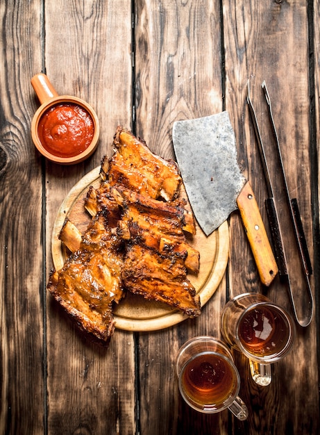 Couper la hache aux côtes du grill avec une bière sur une table en bois.