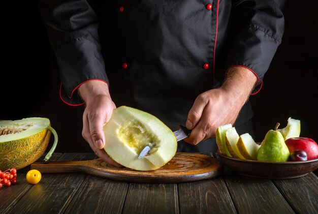 Couper un melon avec un couteau dans la main du chef en petits morceaux pour servir un plat de fruits Concept de régime alimentaire aux fruits Environnement de travail sur la table de cuisine