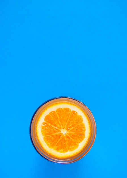 Couper l'orange à la surface du jus d'orange dans un verre sur fond bleu.