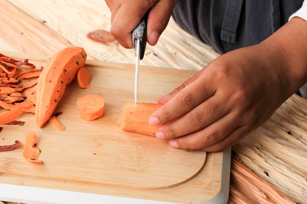 Couper la patate douce à la main asiatique féminine à l'aide d'un couteau sur une table en bois dans la cuisine, processus de fabrication d'aliments traditionnels