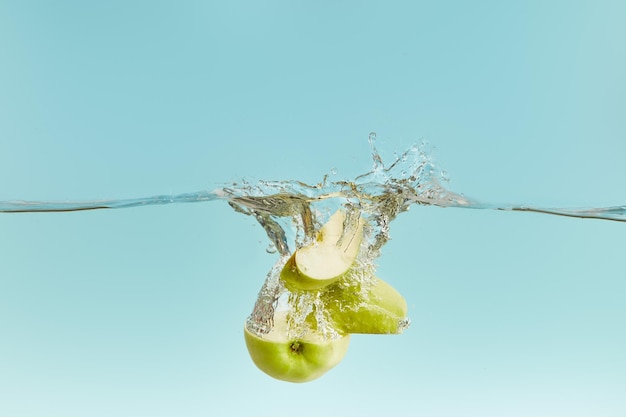 Couper la pomme verte dans l'eau avec des bulles sur fond bleu