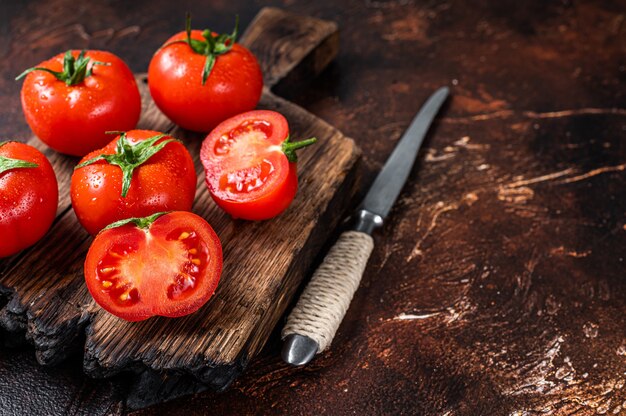 Couper les tomates cerises rouges sur une planche à découper en bois. Fond sombre. Vue de dessus. Copiez l'espace.