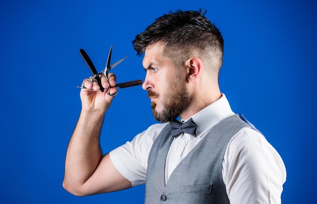 Coupes de cheveux et rasages. Homme barbu avec rasoir et ciseaux dans un salon de coiffure rétro. Hipster avec barbe dans un salon de coiffure rasoir. Homme avec barbe et moustache dans un salon de rasage. Le barbier tient des outils de barbier vintage.