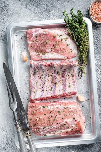 Coupes de porc cru, viande de longe, côtes levées et poitrine sur une assiette de cuisson. Fond blanc. Vue de dessus.