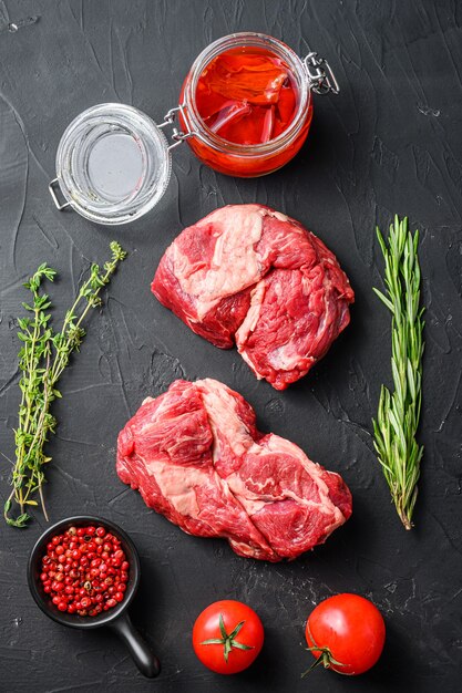 Coupes de steak de rouleau d'oeil de mandrin crues, avec romarin, huile de piment épicée et grains de poivre sur fond noir texturé vue de dessus.