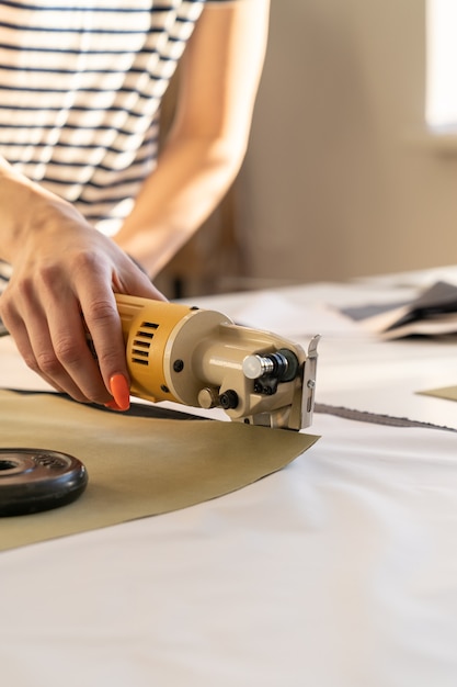 Coupeur électrique pour couper le textile en gros plan du travail manuel des femmes avec du tissu dans la salle de studio d'atelier