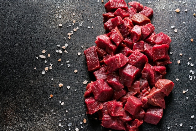 Coupez le bœuf en petits morceaux avec du sel de mer, des herbes séchées et des piments sur fond d'ardoise foncée ou de béton. Vue de dessus.