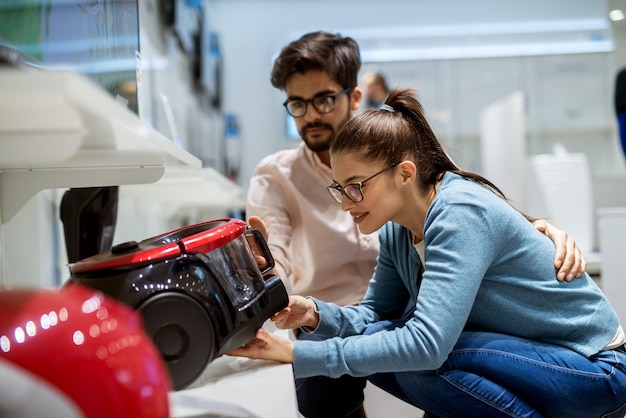 couple accroupi et regardant dans l'aspirateur dans un magasin de technologie.