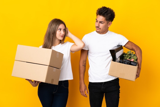 Couple d'adolescents se déplaçant dans une nouvelle maison parmi les boîtes sur bleu ayant des doutes tout en se grattant la tête