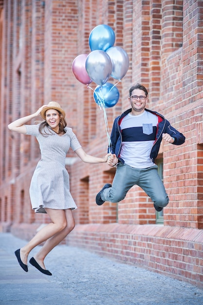 Couple adulte tenant des ballons et sautant lors d'une promenade dans la ville