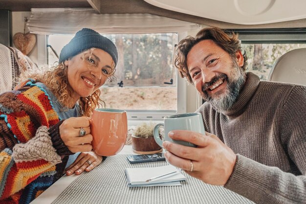 Un couple d'adultes joyeux sourit et profite des vacances de vacances en camping-car avec des tasses à l'intérieur