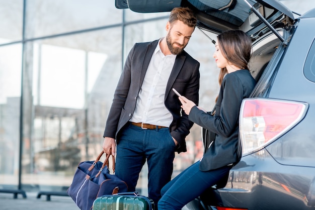 Couple d'affaires assis dans le coffre de la voiture avec valise dans la ville. Voyage d'affaires en voiture concept