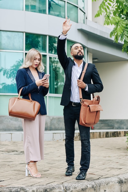 Couple d'affaires debout sur le trottoir, homme attrapant un taxi et ami texto femme