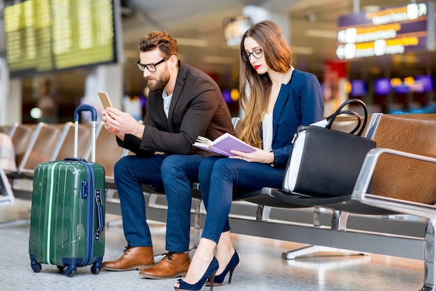 Couple d'affaires élégant assis avec téléphone et livre dans la salle d'attente de l'aéroport. Concept de voyage d'affaires