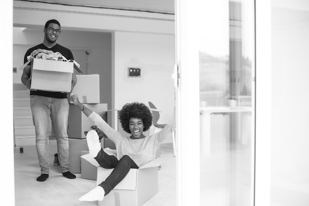 Couple afro-américain assis dans une boîte jouant avec du matériel d'emballage, s'amusant après avoir emménagé dans une nouvelle maison