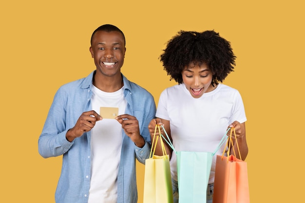 Un couple afro-américain excité avec des sacs d'achat colorés et une carte de crédit