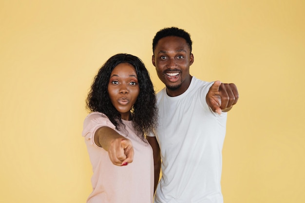 Couple afro-américain réussi pointant vers la caméra dans l'espace de copie de fond jaune studio