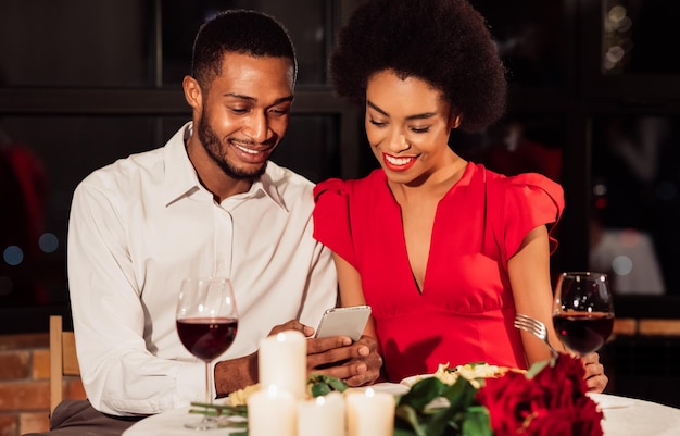 Un couple afro-américain utilise un téléphone portable pendant un rendez-vous dans un restaurant chic.
