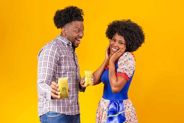 Couple afro-valentin en vêtements festa junina tenant un tamale sur fond jaune