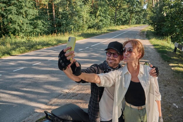 Couple d'âge moyen conduisant une moto s'amusant et prenant un selfie sur un appareil photo de téléphone portable