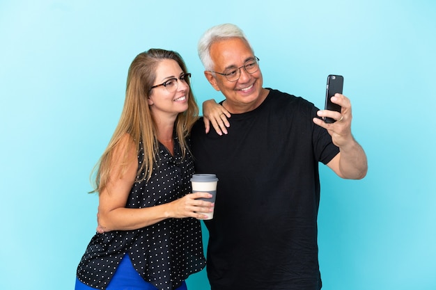 Couple d'âge moyen isolé sur fond bleu faisant un selfie avec le mobile