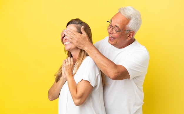 Couple d'âge moyen isolé sur fond jaune couvrant ses yeux pour le surprendre