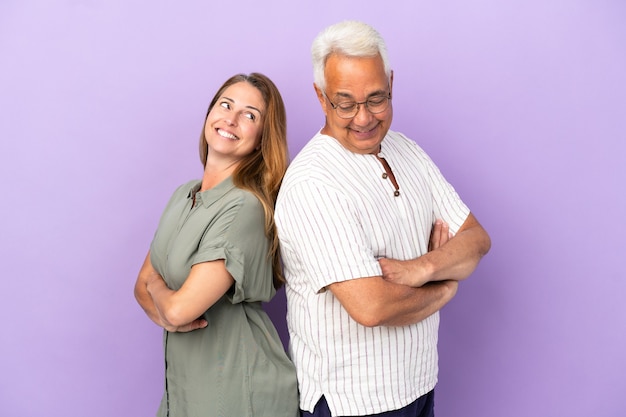 Couple d'âge moyen isolé sur fond violet en gardant les bras croisés en se regardant