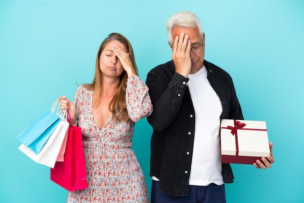 Couple d'âge moyen avec panier et cadeau isolé sur fond bleu avec une expression faciale surprise et choquée