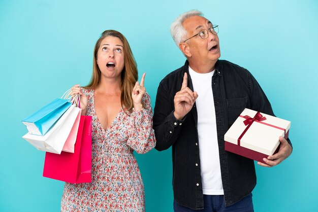 Couple d'âge moyen avec panier et cadeau isolé sur fond bleu pensant à une idée pointant le doigt vers le haut