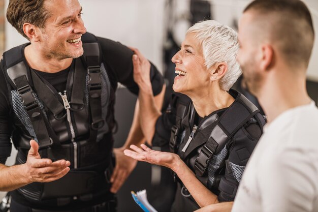 Un couple d'âge moyen parle avec un entraîneur personnel avant l'entraînement EMS dans la salle de sport.