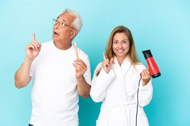 Couple d'âge moyen tenant une sécheuse et une brosse à dents isolées sur fond bleu pensant à une idée pointant le doigt vers le haut