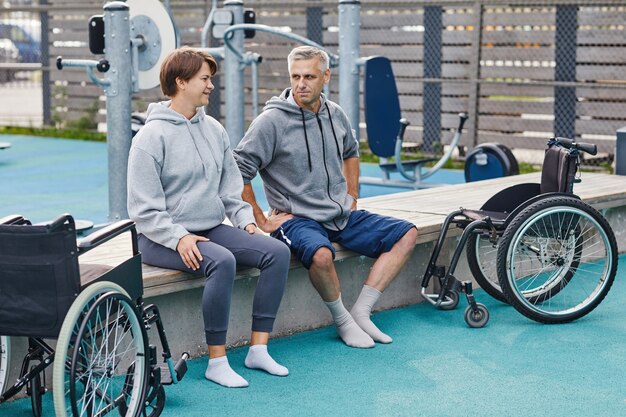 Couple d'âge mûr avec capacité assis sur le banc et parler pendant l'entraînement sportif à l'extérieur