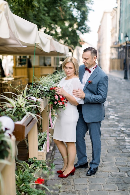 Couple d'âge mûr dans des vêtements à la mode, posant près de décorations de pots de fleurs au café de la ville en plein air