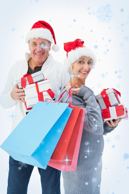 Couple d'âge mûr festif en vêtements d'hiver tenant des cadeaux et des sacs contre les chutes de neige