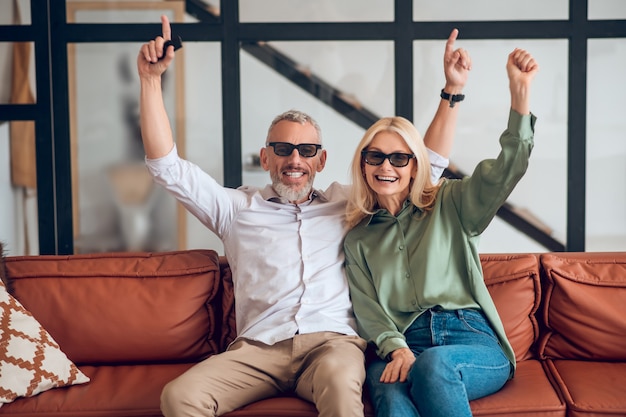 Couple d'âge mûr à lunettes de soleil assis sur le canapé et se sentir joyeux