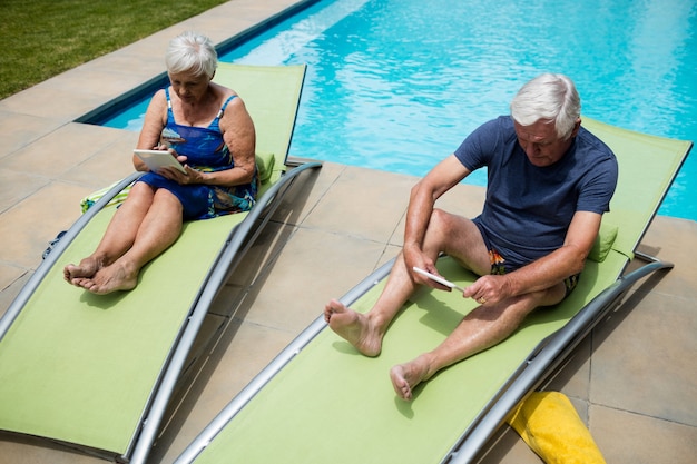 Couple à l'aide de tablette numérique sur une chaise longue au bord de la piscine