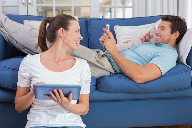 Couple à l&#39;aide de tablette numérique et téléphone portable dans le salon