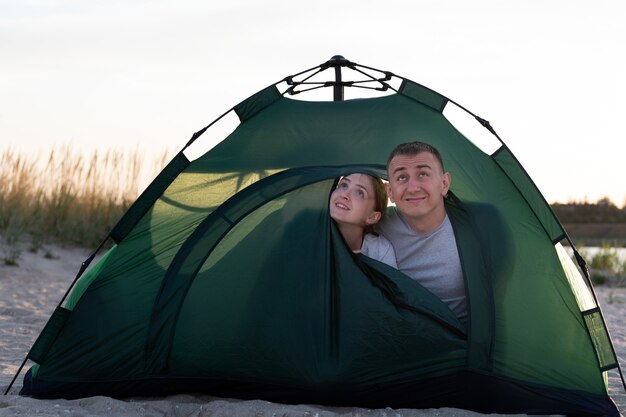 Couple aimant furtivement hors d'une grande tente verte en camping