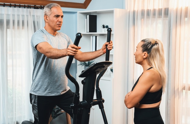 Couple d'aînés actifs qui courent sur une machine à courir elliptique à la maison ensemble comme forme physique, mode de vie sain et soins corporels après la retraite pour le retraité Clout