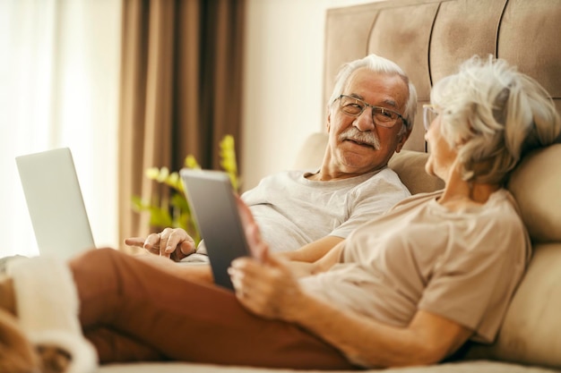 Un couple d'aînés est sur Internet et est allongé dans une chambre.