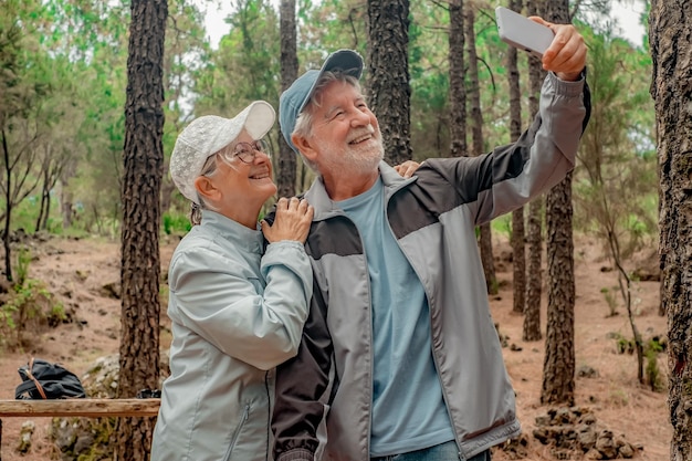 Un couple d'aînés joyeux dans une journée de randonnée dans les bois en train de regarder un smartphone pour prendre un selfie