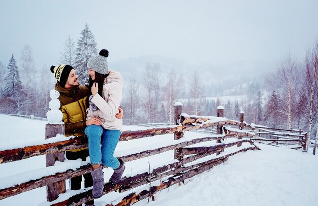 couple a l&#39;air drôle assis sur la clôture avec bonhomme de neige