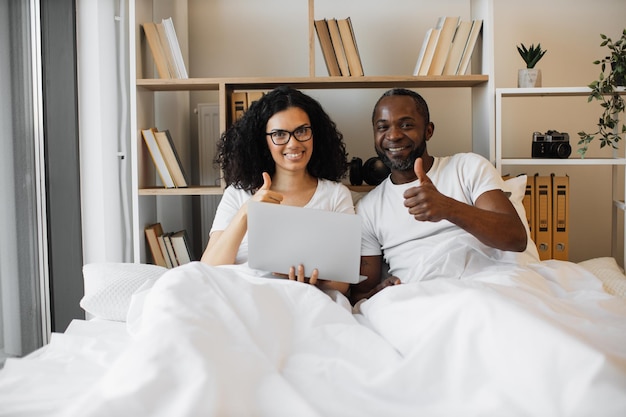 Couple allongé dans son lit avec un ordinateur portable et montrant les pouces vers le haut