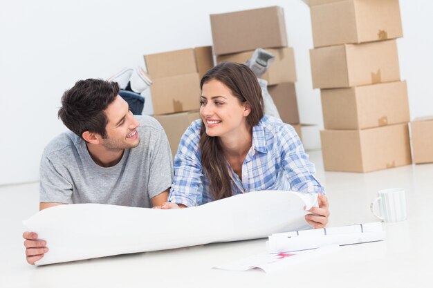 Photo couple allongé sur le sol et tenant des plans de maison