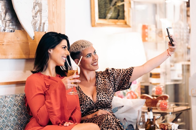 Photo un couple d'amies prend un selfie assis en buvant dans un bar