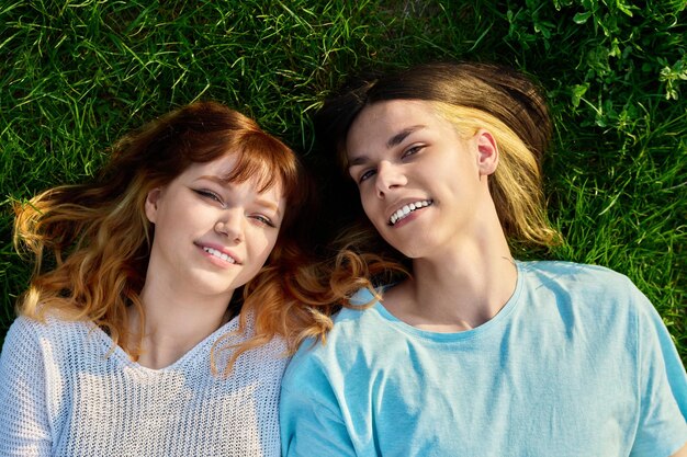 Un couple d'amis adolescents regardent la caméra sur un fond d'herbe verte. Un garçon et une fille heureux de 17 et 18 ans allongés sur la pelouse. Vue supérieure de l'amitié jeunesse, style de vie des jeunes, concept.