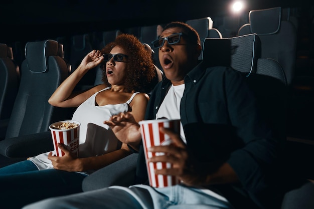 Un couple d'amis amoureux regardant un film avec du pop-corn au cinéma