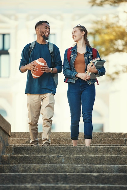 Couple d'amis ou d'étudiants marchant dans les escaliers d'un collège universitaire ou d'un campus avec des livres ou un ballon de football Éducation sportive ou homme et femme avec réseau de communication ou examen d'études scolaires